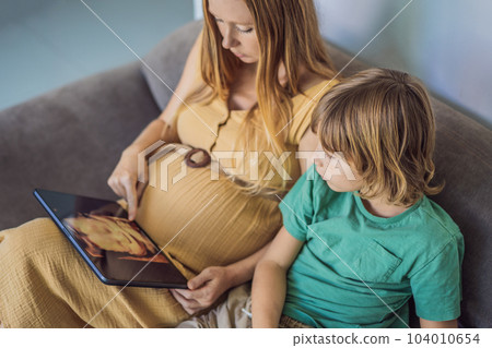 Mom and her son looking on ultrasound image of his unborn baby brother on mothers tablet. Concept of healthcare and family happiness expecting baby Mom and her son looking on ultrasound image of his unborn baby brother on mothers tablet. Concept of healthcare and family happiness expecting baby 104010654