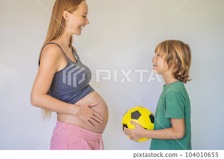 Amusing son. Pregnant beautiful woman amusing her little son while putting yellow ball under his green shirt Amusing son. Pregnant beautiful woman amusing her little son while putting yellow ball under his green shirt 104010655