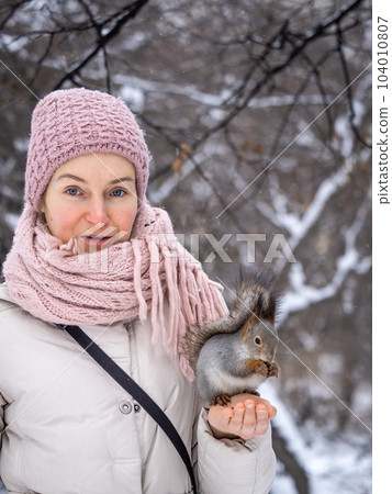 Girl feeds a squirrel with nuts at winter. Caring for animals in winter or autumn. Girl feeds a squirrel with nuts at winter. Caring for animals in winter or autumn. 104010807