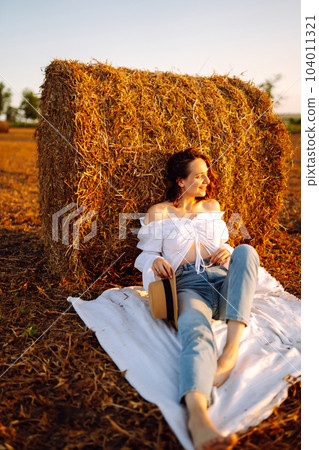 Happy woman near haystack at sunset. Fashion concept. Nature, vacation, relax and lifestyle. Happy woman near haystack at sunset. Fashion concept. Nature, vacation, relax and lifestyle. 104011321