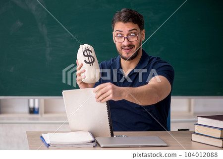 Young male teacher holding moneybag in the classroom 104012088