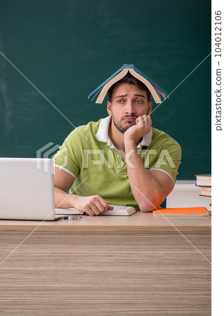 Young male student sitting in front of green board 104012106