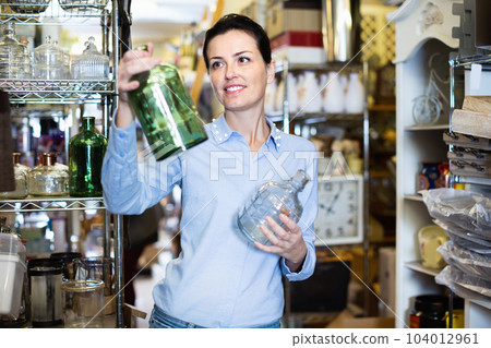 Adult woman buyer shopping glass jar in shop with goods for decor 104012961