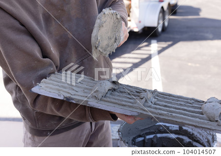 Man applying spreading wet cement adhesive before applying tiles installation with worker using trowels tools Man applying spreading wet cement adhesive before applying tiles installation with worker using trowels tools 104014507