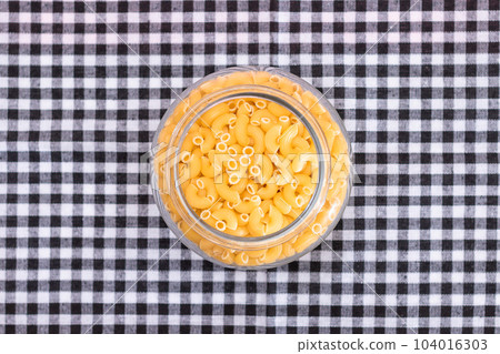 Uncooked Chifferi Rigati Pasta in Glass Jar on Black Checkered Towel 104016303