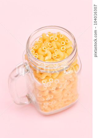 Uncooked Chifferi Rigati Pasta in Glass Jar on Pink Background Uncooked Chifferi Rigati Pasta in Glass Jar on Pink Background 104016307