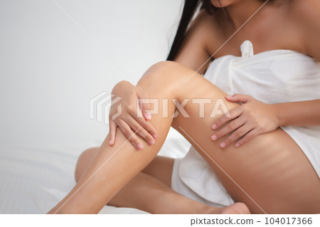 Body skincare treatment concept. woman applying skin cream leg area sitting in dressing room. 104017366