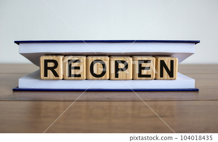Concept word 'reopen' on wooden cubes between pages of a book on a beautiful wooden table. White background. Business concept. 104018435