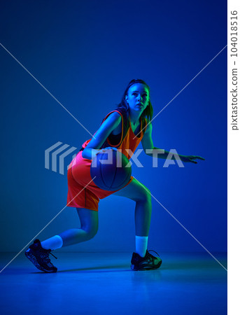Motivation to win. Young female basketball player in motion during game against blue studio background in neon light 104018516