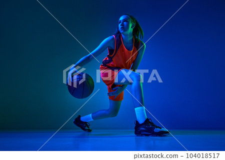 Motivation to win. Young female basketball player in motion during game against blue studio background in neon light 104018517