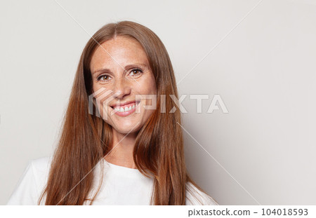 Happy excited mid adult woman with long healthy brown hair smiling, indoor studio portrait.  104018593
