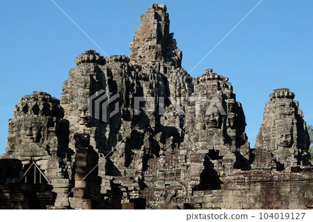 Majestic stone towers of the Bayon Temple, a Khmer architectural marvel, under a blue sky. Majestic stone towers of the Bayon Temple, a Khmer architectural marvel, under a blue sky. 104019127