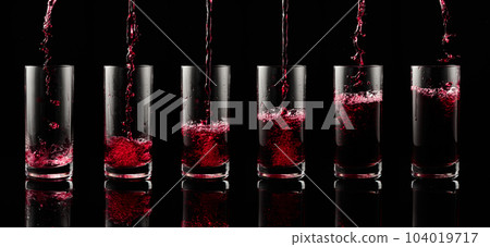 Pouring red juice into a glass on a black background. 104019717