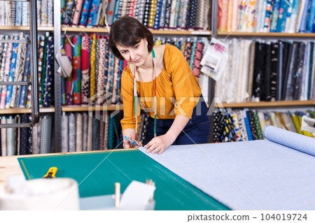 Female seller measuring and cutting off piece of textile Female seller measuring and cutting off piece of textile 104019724