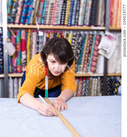 Female seller measuring and cutting off piece of textile Female seller measuring and cutting off piece of textile 104019777
