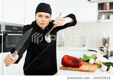 Young woman chef in black uniform posing with big knife Young woman chef in black uniform posing with big knife 104019819