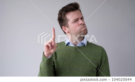 European young man shakes his head in disagreement and says no, pointing his finger upwards 104020844