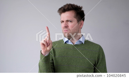 European young man shakes his head in disagreement and says no, pointing his finger upwards 104020845