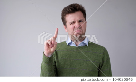 European young man shakes his head in disagreement and says no, pointing his finger upwards 104020846
