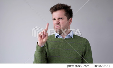 European young man shakes his head in disagreement and says no, pointing his finger upwards 104020847