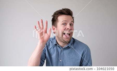 European young man waves his hand, greets his friends. 104021050