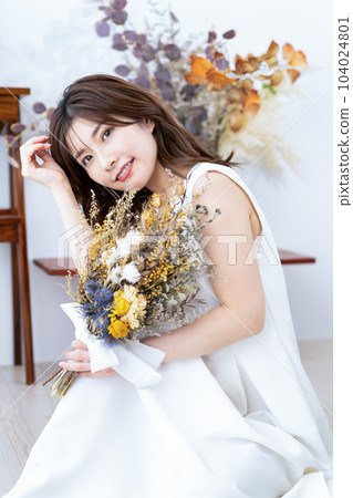 一個穿著白色連衣裙的女人拿著一束乾花 104024801