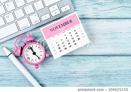 The November 2023 Monthly calendar year and alarm clock with keyboard computer on wooden background. 104025158
