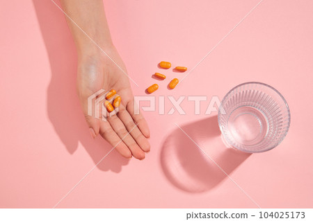 Orange pills are arranged on the pink background with a glass of water and in a hand. Concept of healthy lifestyle 104025173
