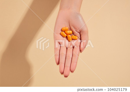 Minimal scene of a hand featuring some orange pills on a beige background. Concept of medicine and health support 104025179