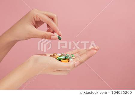 A stack of many tablets, capsules and pills on a female hand against pink background. Tablets in hand of patient. Medical concept 104025200