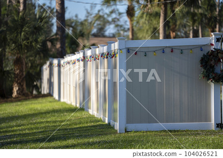 White vinyl picket fence on green lawn surrounding property grounds for backyard protection and privacy 104026521