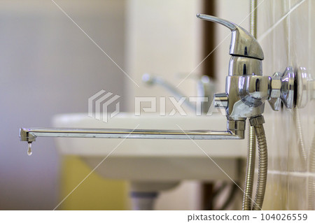 Water tap, chrome stainless metal faucet with running water stream connected to shower stall tiled wall, mixer cold hot water on blurred bathroom background. Modern home interior. Water tap, chrome stainless metal faucet with running water stream connected to shower stall tiled wall, mixer cold hot water on blurred bathroom background. Modern home interior. 104026559