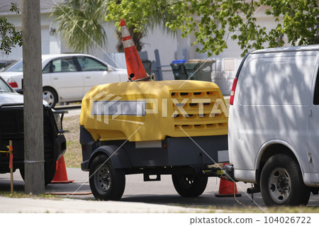 Utility van with yellow compressor trailer with jackhammer machine on road construction site 104026722