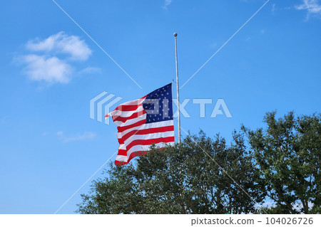 USA national flag waving lowered to half mast on wind against blue sky. American stars and stripes spangled banner as symbol of democracy 104026726