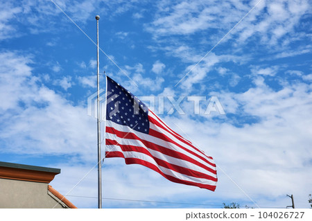 USA national flag waving lowered to half mast on wind against blue sky. American stars and stripes spangled banner as symbol of democracy USA national flag waving lowered to half mast on wind against blue sky. American stars and stripes spangled banner as symbol of democracy 104026727