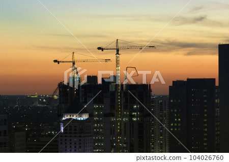 Tower lifting cranes at high residential apartment building construction site at sunset. Real estate development in Miami urban area 104026760