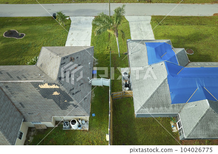 Top view of leaking house roof covered with protective tarp sheets against rain water leaks until replacement of asphalt shingles. Damage of building rooftop as aftermath of hurricane Ian in Florida Top view of leaking house roof covered with protective tarp sheets against rain water leaks until replacement of asphalt shingles. Damage of building rooftop as aftermath of hurricane Ian in Florida 104026775
