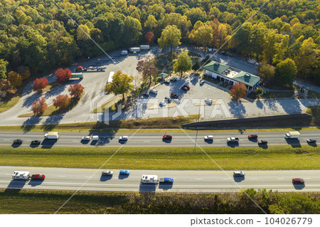 Top view of large rest area near busy multilane american freeway with fast moving cars and trucks. Recreational resting place during interstate traveling Top view of large rest area near busy multilane american freeway with fast moving cars and trucks. Recreational resting place during interstate traveling 104026779