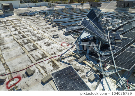Top view of destroyed by hurricane Ian photovoltaic solar panels mounted on industrial building roof for producing green ecological electricity. Consequences of natural disaster in Florida 104026789