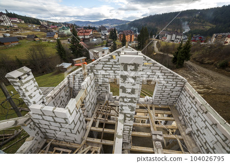 Top view of cottage walls and chimneys made of large white hollow foam insulation blocks and wooden flooring frame on mountain village summer landscape background. Construction and masonry concept. 104026795