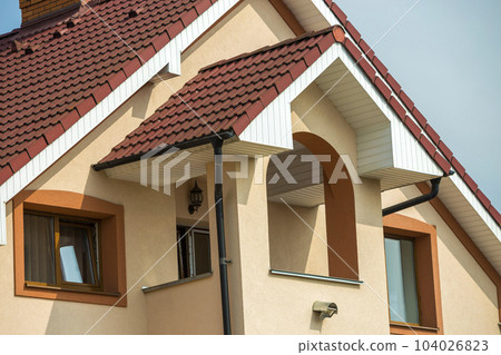 Top detail front of big modern expensive residential family cottage with shingled brown roof, brick chimney, stucco walls on blue sky background. Real estate investment, comfortable dwelling concept. Top detail front of big modern expensive residential family cottage with shingled brown roof, brick chimney, stucco walls on blue sky background. Real estate investment, comfortable dwelling concept. 104026823