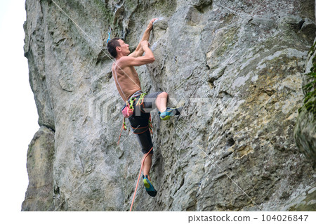 Strong male climber climbing steep wall of rocky mountain. Sportsman overcoming difficult route. Engaging in extreme sports hobby concept. 104026847