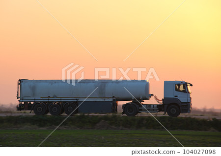 Semi-truck with tipping cargo trailer transporting sand from quarry driving on highway hauling goods in evening. Delivery transportation and logistics concept Semi-truck with tipping cargo trailer transporting sand from quarry driving on highway hauling goods in evening. Delivery transportation and logistics concept 104027098
