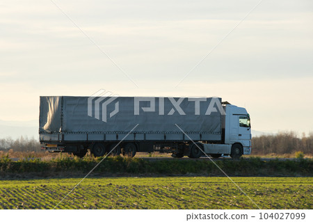 Semi-truck with cargo trailer driving on highway hauling goods in evening. Delivery transportation and logistics concept 104027099