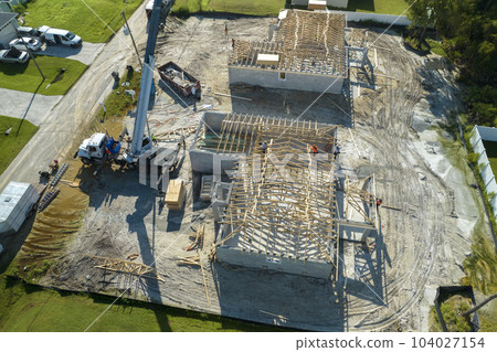 Professional builders and crane truck working on roof construction of unfinished suburban home with wooden frame structure in Florida rural area. Concept of housing development in America 104027154