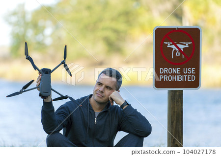 Operator is preparing to fly his quadcopter in national park no drone area. Man unlawfully using his UAV near restriction notice sign 104027178