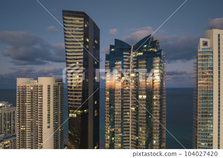 Night urban landscape of downtown district in Sunny Isles Beach city in Florida, USA. Skyline with brightly illuminated high skyscraper buildings in modern american megapolis 104027420