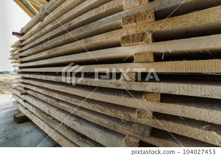 Neatly piled long stack of wooden boards inside attic room under construction. 104027453