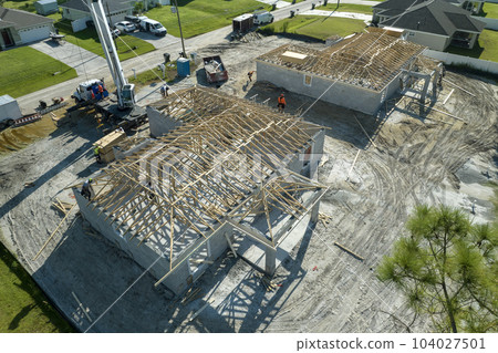 Lifting crane truck and builders working on roof construction of unfinished residential house with wooden frame structure in Florida suburban area. Housing development concept 104027501