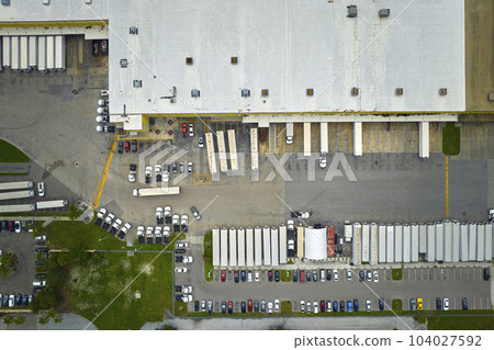 High angle view of big commercial shipping center with many freight trucks unloading and uploading goods for further distribution. Global economy concept High angle view of big commercial shipping center with many freight trucks unloading and uploading goods for further distribution. Global economy concept 104027592